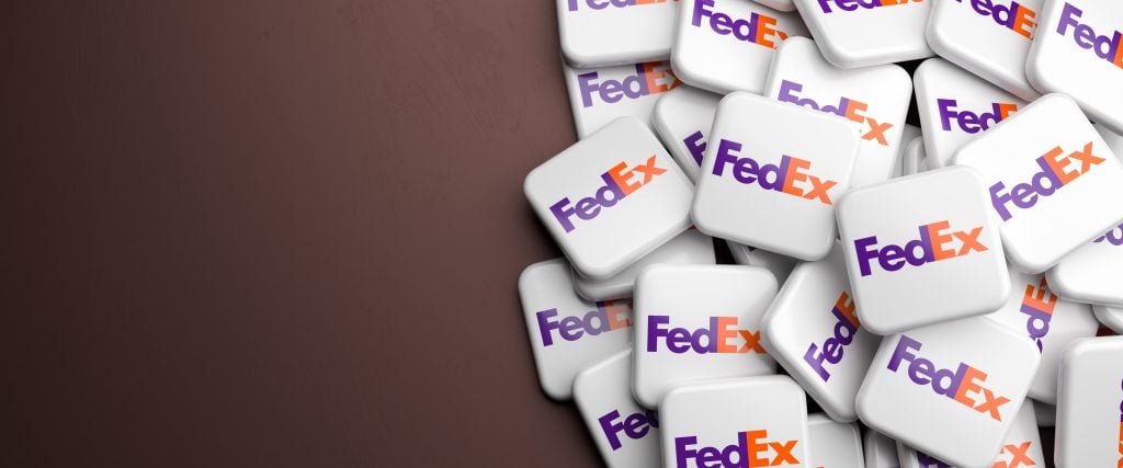 Logos of the shipping and delivery company FedEx Corporation on a heap on a table. Copy space. Web banner format.