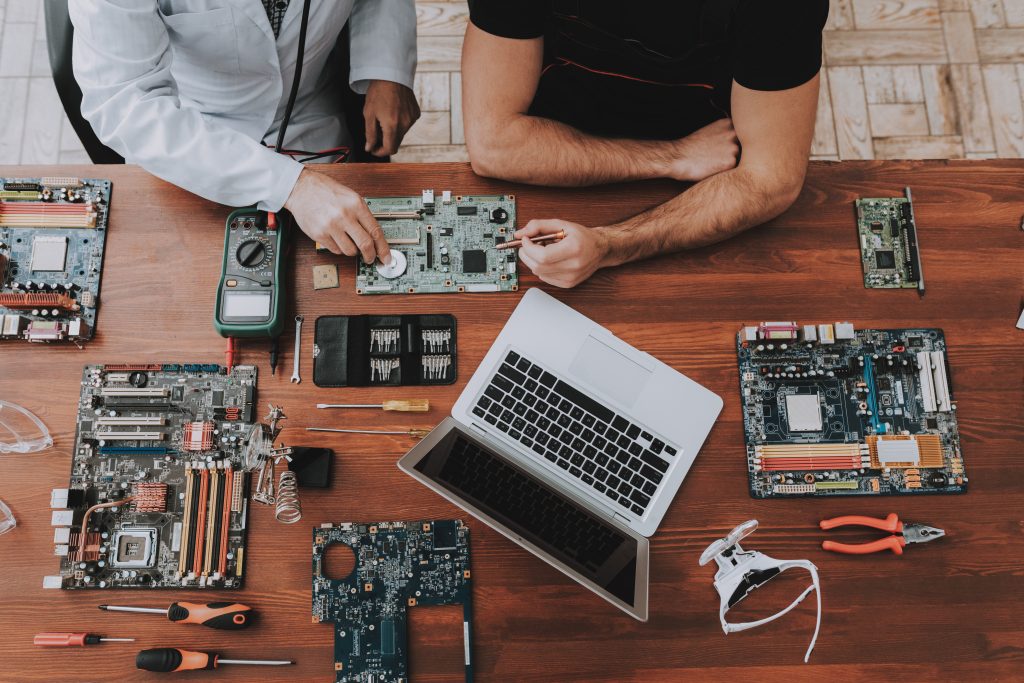 Two Men with Motherboars and Tools on Wooden Table. Modern Workshop Concept. Manufacturing Instrument. Modern Tools Concept. Electronic Devices Concept. Mobile Device Hardware. Wooden Desk.